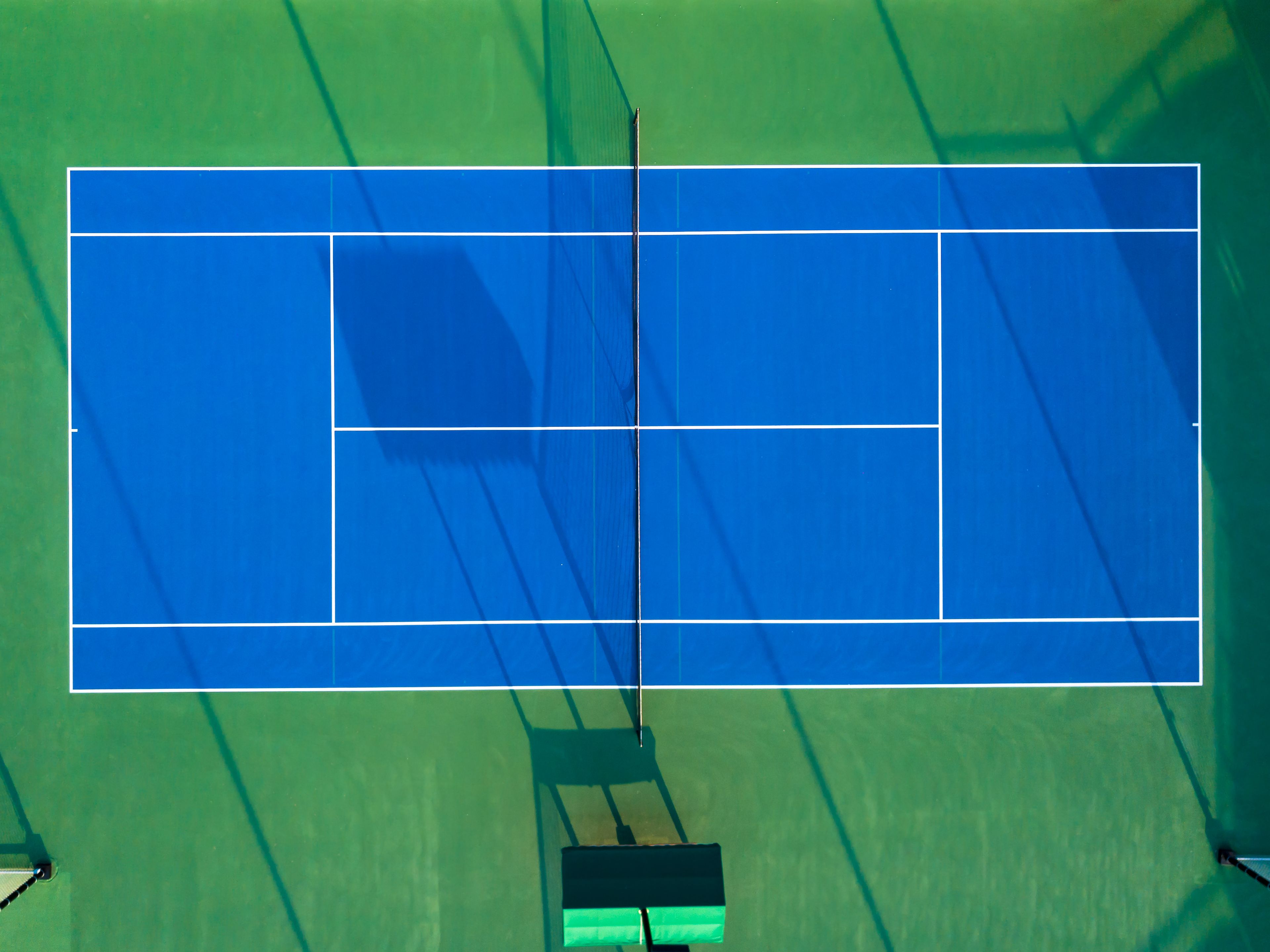 Aerial view of a blue tennis court framed by green playing surface